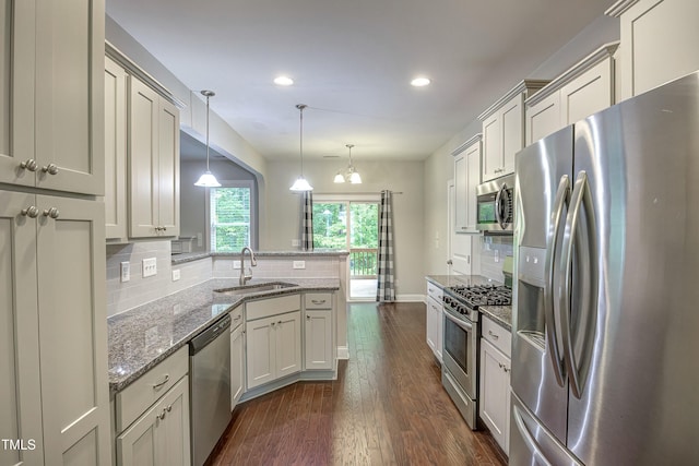 kitchen featuring stainless steel appliances, a peninsula, a sink, decorative backsplash, and dark wood finished floors