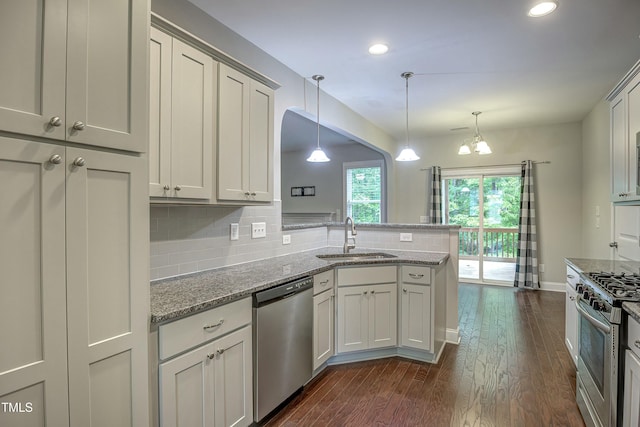 kitchen featuring a peninsula, a sink, appliances with stainless steel finishes, tasteful backsplash, and dark wood finished floors