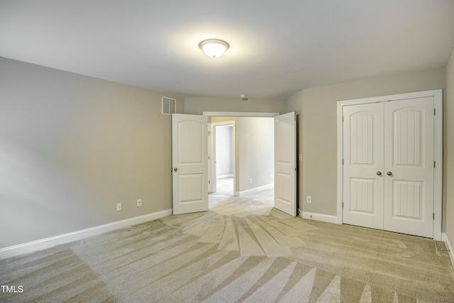 unfurnished bedroom with a closet, visible vents, light carpet, and baseboards