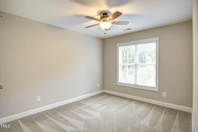 spare room with a ceiling fan, light colored carpet, visible vents, and baseboards