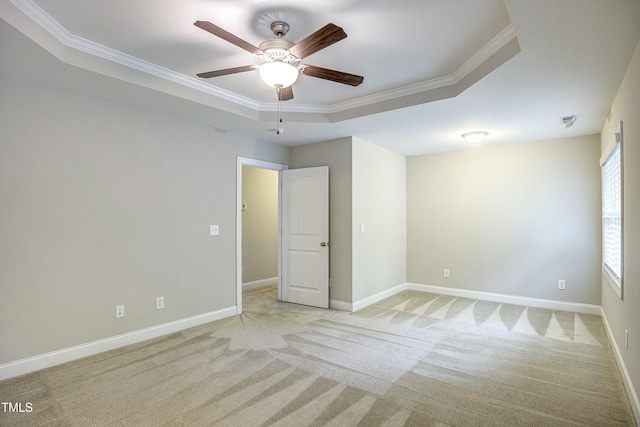 spare room featuring light carpet, baseboards, ceiling fan, ornamental molding, and a tray ceiling