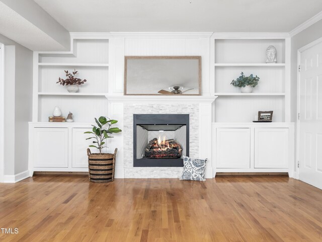 living room featuring built in shelves, light wood-type flooring, a fireplace, and a ceiling fan