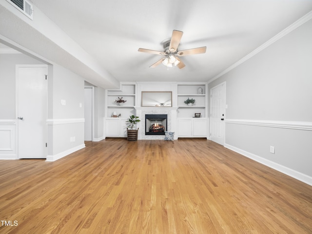 unfurnished living room with built in shelves, light wood-type flooring, a warm lit fireplace, and crown molding