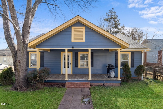 bungalow-style home with a front yard, covered porch, roof with shingles, and fence