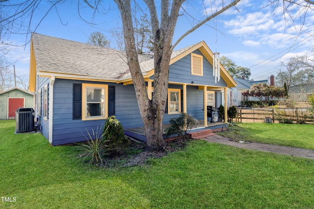 bungalow featuring a shingled roof, fence, a front lawn, and central AC unit