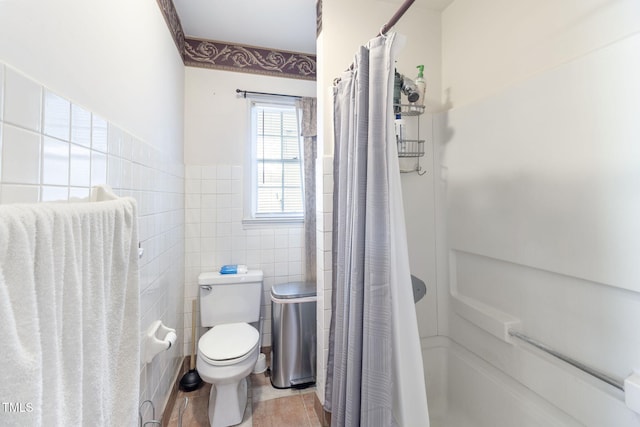bathroom with wainscoting, toilet, a shower with shower curtain, tile patterned flooring, and tile walls