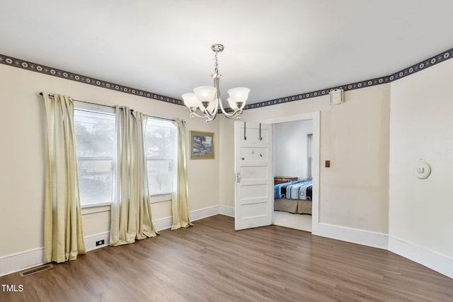 unfurnished dining area with an inviting chandelier, baseboards, visible vents, and wood finished floors
