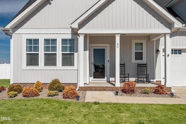 property entrance featuring a yard, a shingled roof, covered porch, board and batten siding, and a garage