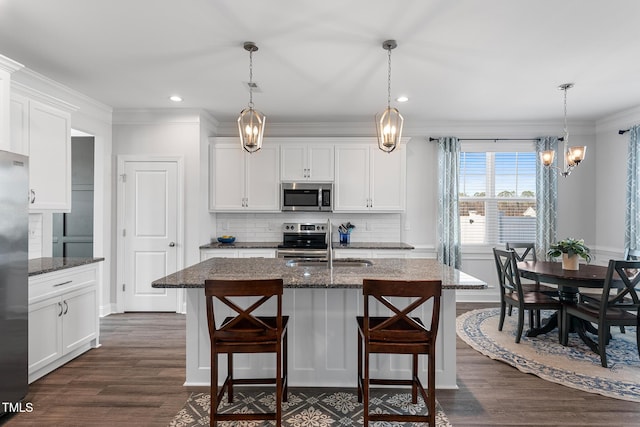 kitchen featuring stainless steel appliances, tasteful backsplash, ornamental molding, white cabinetry, and a kitchen breakfast bar