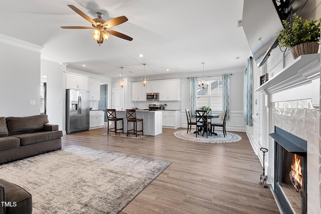 living room featuring ornamental molding, a tiled fireplace, wood finished floors, and a ceiling fan