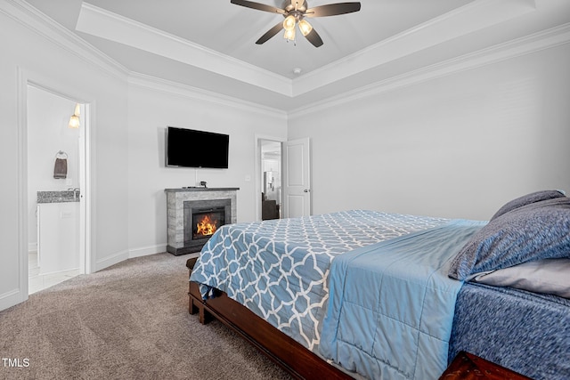 carpeted bedroom with a lit fireplace, crown molding, a tray ceiling, and baseboards