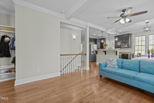 living room with beam ceiling, wood finished floors, baseboards, and ornamental molding