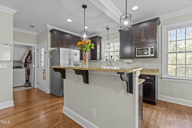 kitchen with dark brown cabinets, a kitchen bar, ornamental molding, appliances with stainless steel finishes, and washer / clothes dryer