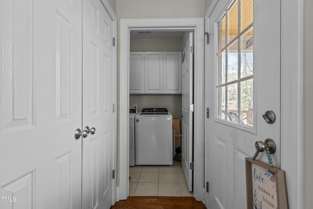 clothes washing area featuring washing machine and dryer, light tile patterned flooring, and cabinet space