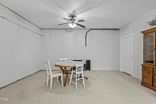 dining space with a ceiling fan, carpet, and concrete block wall