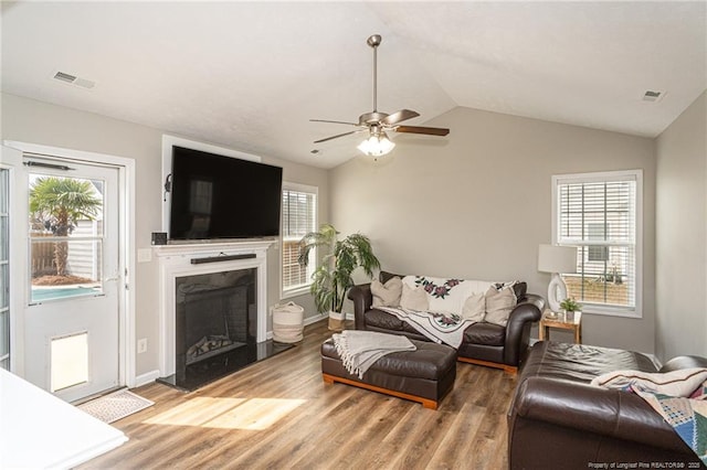 living room featuring lofted ceiling, a fireplace with raised hearth, a wealth of natural light, and wood finished floors