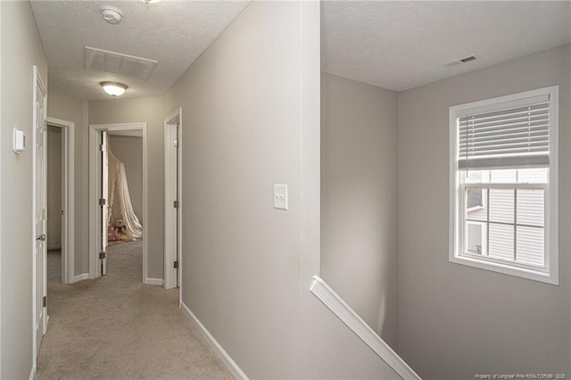 hall featuring light carpet, visible vents, a textured ceiling, and an upstairs landing