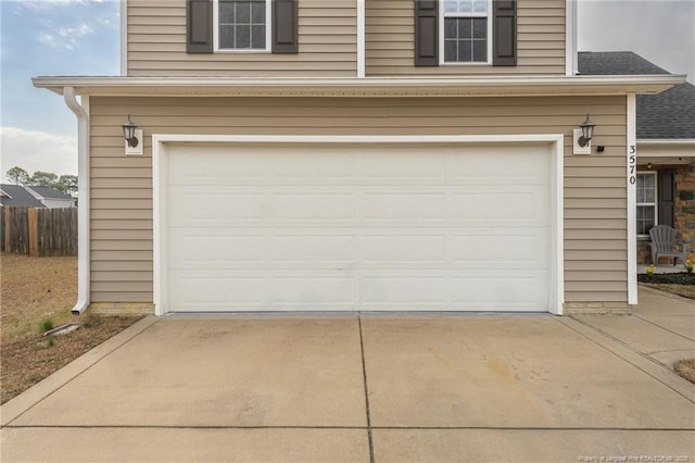 garage with concrete driveway and fence