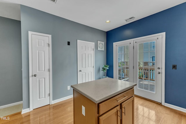 kitchen with light wood-type flooring, a center island, visible vents, and baseboards