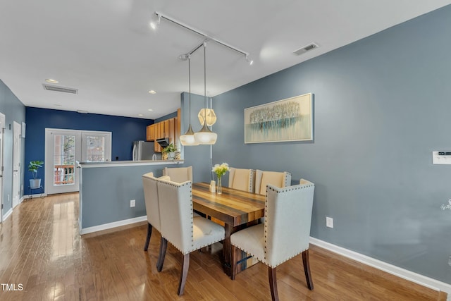 dining space featuring rail lighting, visible vents, baseboards, and wood finished floors