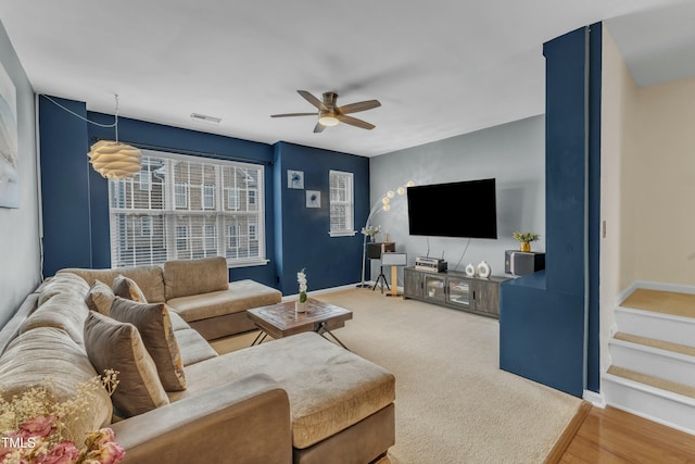 living room featuring ceiling fan, carpet flooring, visible vents, baseboards, and stairs