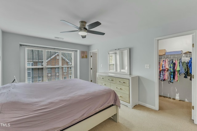 bedroom with a closet, light colored carpet, a spacious closet, ceiling fan, and baseboards