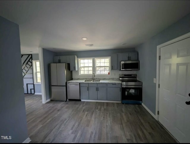 kitchen with wood finished floors, a sink, baseboards, light countertops, and appliances with stainless steel finishes