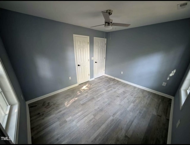 unfurnished bedroom featuring baseboards, visible vents, a ceiling fan, dark wood-type flooring, and two closets