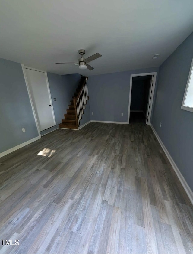 unfurnished living room with ceiling fan, stairway, wood finished floors, and baseboards