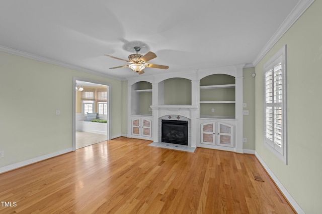 unfurnished living room featuring built in features, a fireplace with flush hearth, light wood-style floors, ornamental molding, and baseboards