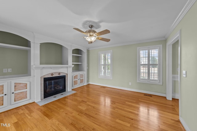 unfurnished living room featuring built in shelves, a fireplace, visible vents, light wood-style flooring, and ornamental molding