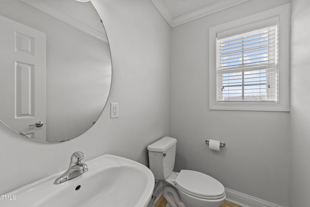 half bathroom with crown molding, baseboards, a sink, and toilet