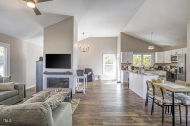 living area with a fireplace, vaulted ceiling, dark wood finished floors, and ceiling fan with notable chandelier