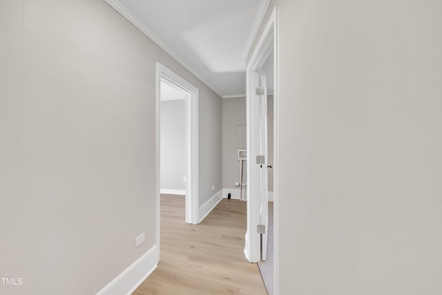 corridor with light wood finished floors, ornamental molding, and baseboards