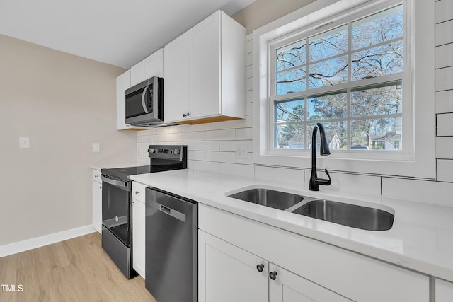 kitchen featuring light countertops, decorative backsplash, appliances with stainless steel finishes, a sink, and light wood-type flooring