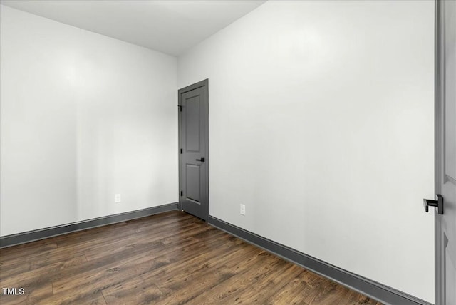 empty room featuring baseboards and dark wood-type flooring