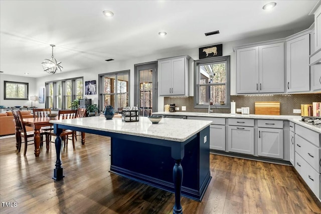 kitchen with dark wood-type flooring, backsplash, a wealth of natural light, and a center island