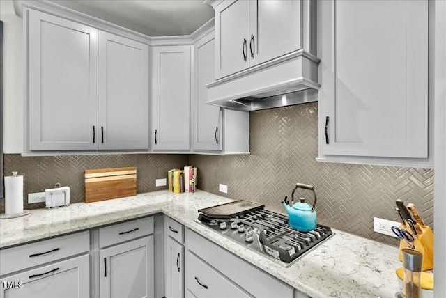 kitchen featuring tasteful backsplash, custom range hood, stainless steel gas stovetop, and light stone counters