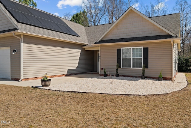 view of front facade with a shingled roof, a front yard, an attached garage, and solar panels