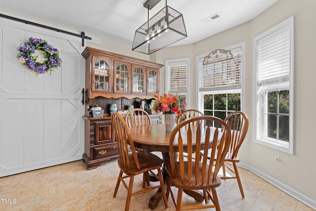 dining area with a barn door, a textured ceiling, visible vents, and baseboards