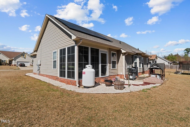 rear view of house with solar panels, a yard, a trampoline, and a sunroom