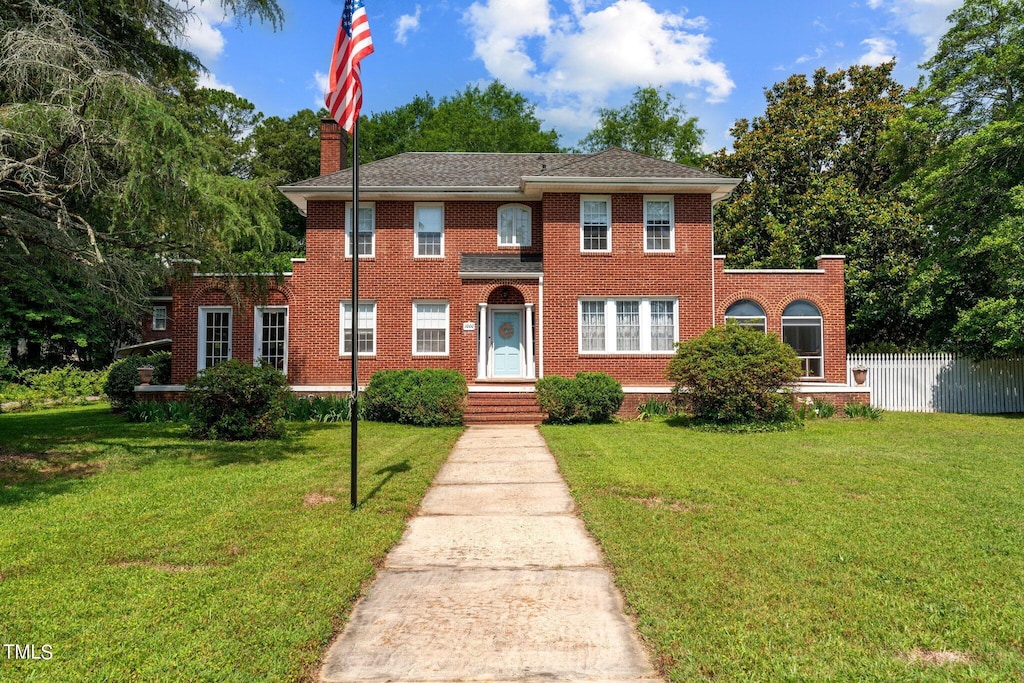 view of front facade with a front yard, brick siding, fence, and a chimney