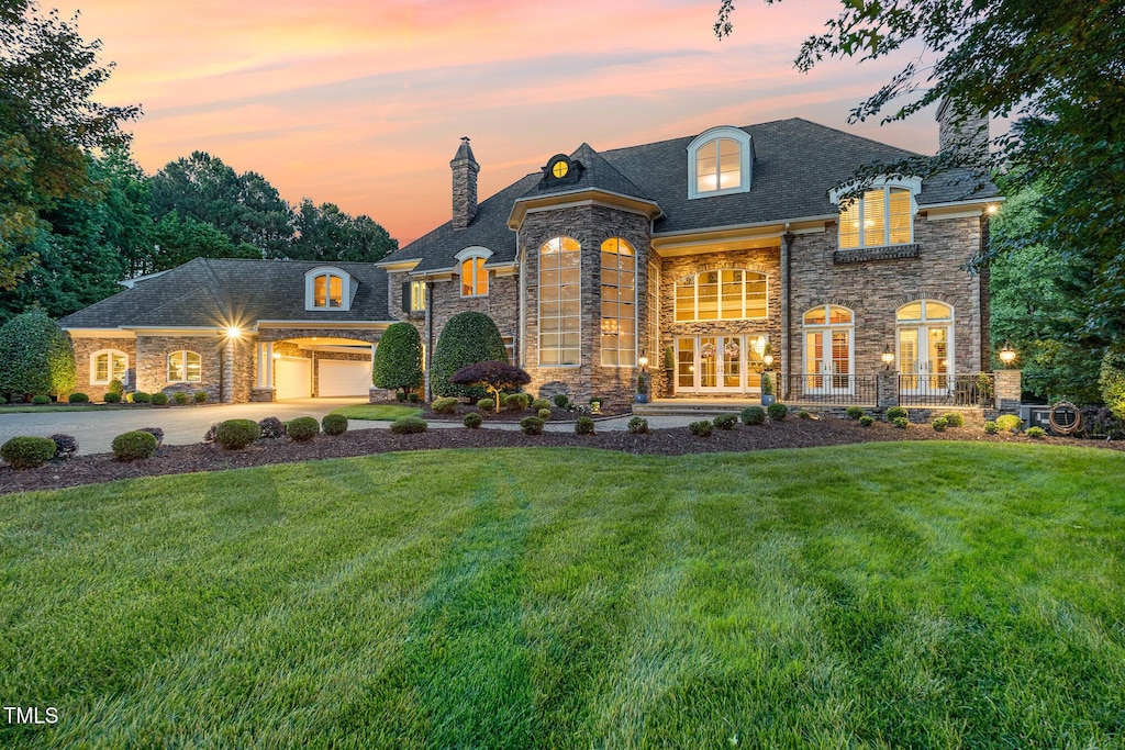 french country home featuring a garage, concrete driveway, french doors, a chimney, and a front yard