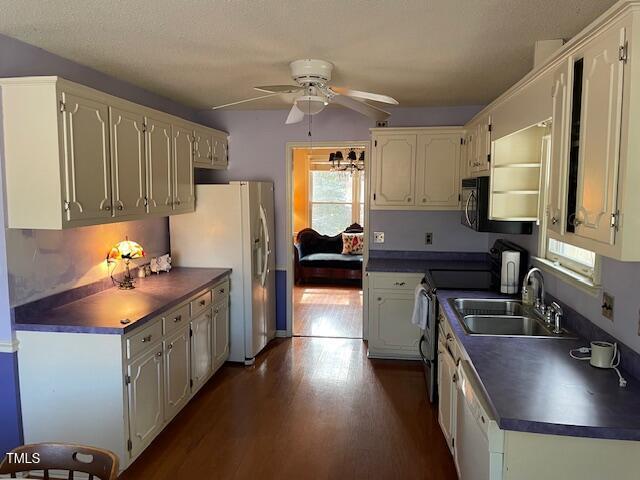 kitchen with dark countertops, white appliances, dark wood-style flooring, and a sink