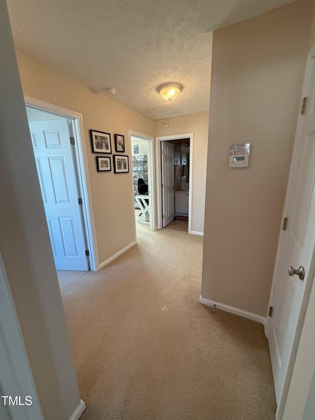 hall with light carpet, a textured ceiling, and baseboards