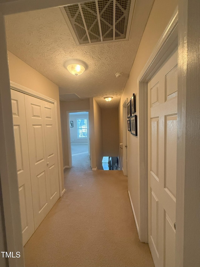 hallway featuring light colored carpet, visible vents, a textured ceiling, and baseboards