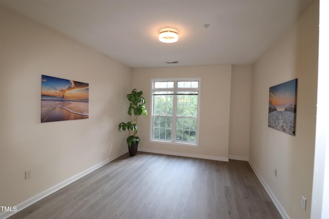 spare room featuring baseboards, visible vents, and wood finished floors