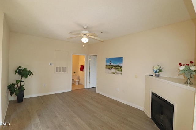 unfurnished living room featuring visible vents, light wood-style flooring, a ceiling fan, a glass covered fireplace, and baseboards