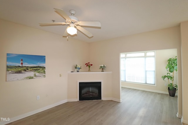 unfurnished living room with ceiling fan, a fireplace, wood finished floors, and baseboards