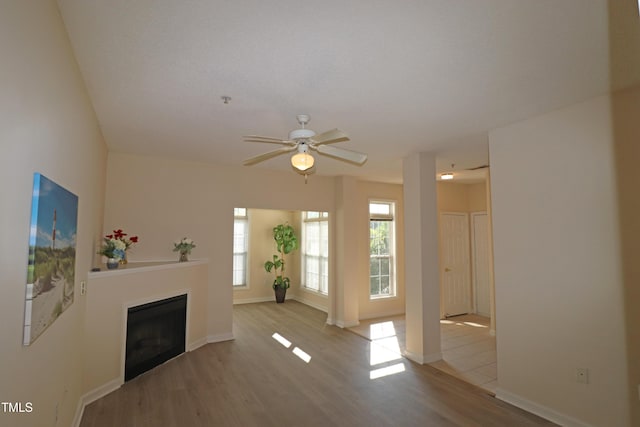 unfurnished living room with a fireplace, wood finished floors, a ceiling fan, and baseboards